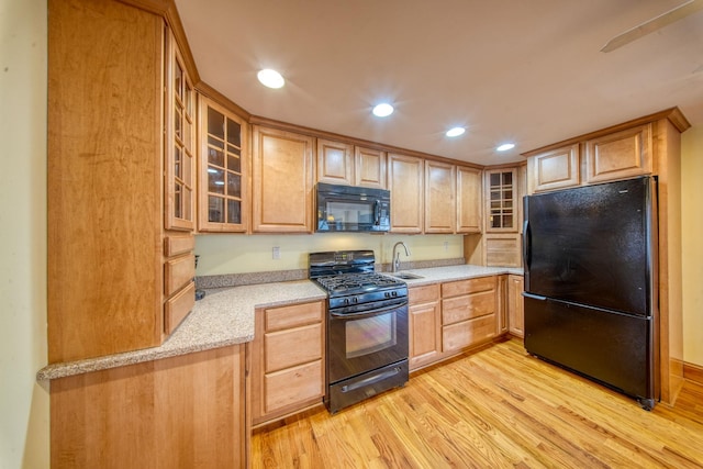 kitchen featuring black appliances, recessed lighting, glass insert cabinets, and light wood-style floors