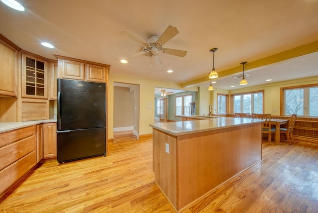 kitchen featuring light stone counters, recessed lighting, light wood-style flooring, glass insert cabinets, and freestanding refrigerator