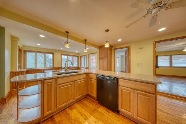 kitchen featuring black dishwasher, light stone counters, decorative light fixtures, light wood-style floors, and a sink