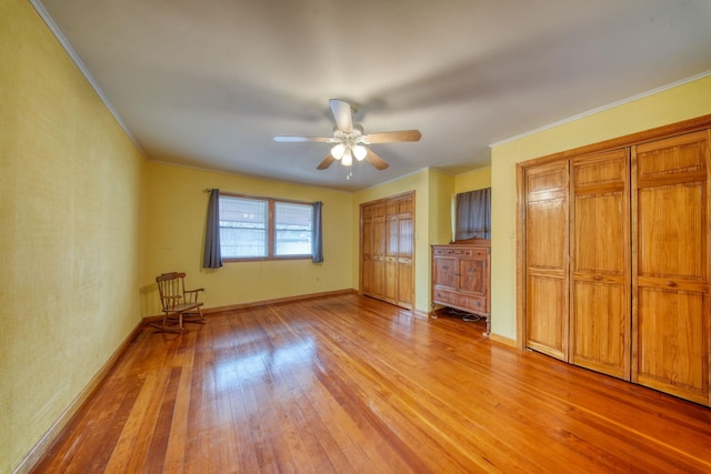 unfurnished bedroom with ornamental molding, two closets, light wood-style flooring, and baseboards