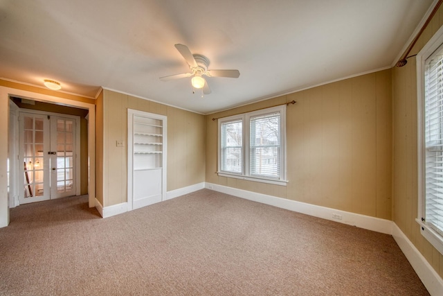 carpeted empty room with built in features, french doors, ornamental molding, a ceiling fan, and baseboards