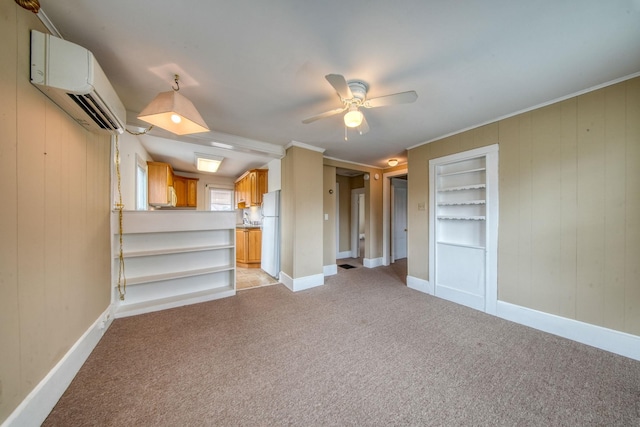 unfurnished living room featuring ceiling fan, built in shelves, light colored carpet, baseboards, and an AC wall unit