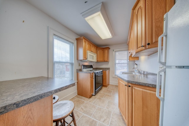 kitchen featuring white appliances, light tile patterned floors, dark countertops, a breakfast bar area, and a sink