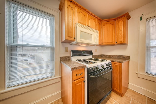 kitchen featuring a healthy amount of sunlight, white microwave, light tile patterned flooring, and gas range