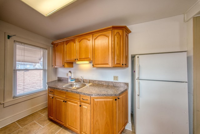 kitchen featuring dark countertops, brown cabinets, a sink, and freestanding refrigerator