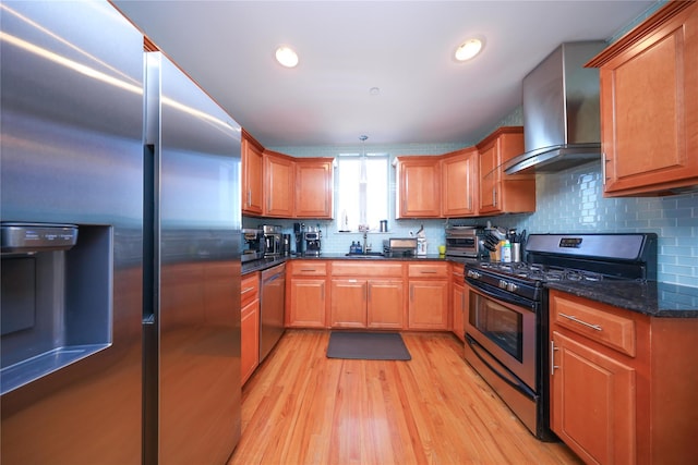 kitchen featuring light wood finished floors, decorative backsplash, appliances with stainless steel finishes, and wall chimney range hood