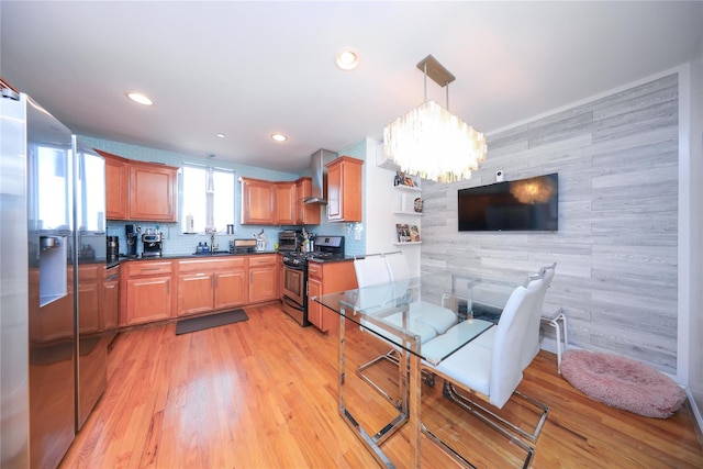 kitchen with light wood-style flooring, gas range, dark countertops, and wall chimney exhaust hood