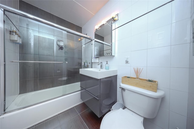 full bathroom featuring tile patterned floors, toilet, shower / bath combination with glass door, tile walls, and vanity