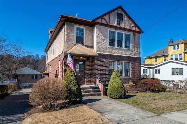 tudor home featuring brick siding, stone siding, and a front lawn