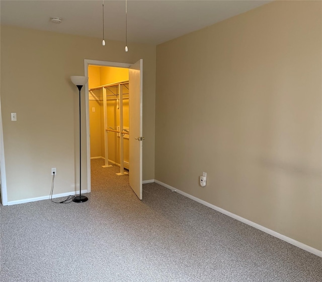 unfurnished bedroom featuring a spacious closet, a closet, baseboards, and carpet floors