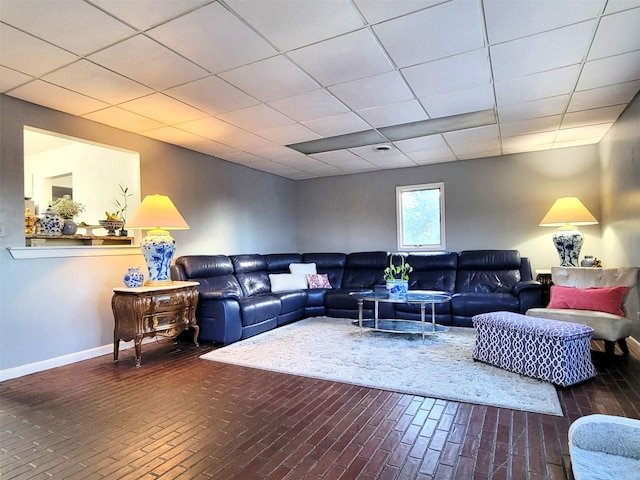 living area featuring brick floor, a paneled ceiling, and baseboards