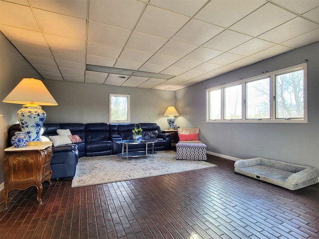 living area featuring brick floor, a paneled ceiling, and baseboards