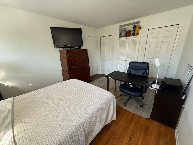 bedroom featuring lofted ceiling, two closets, and wood finished floors