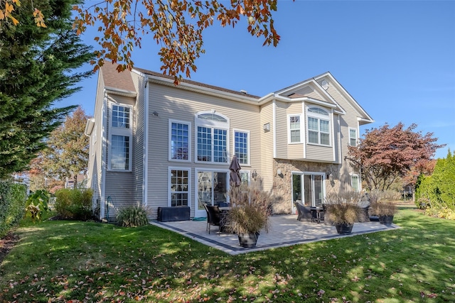 back of property with stone siding, a lawn, and a patio