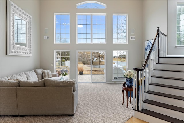 carpeted living area featuring stairs, a towering ceiling, and visible vents