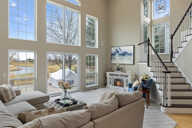 living area with baseboards, stairs, a high ceiling, and a glass covered fireplace