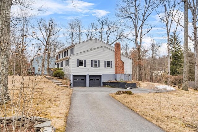 view of property exterior featuring driveway, a chimney, and an attached garage