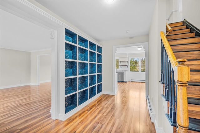 hall with light wood-type flooring, a baseboard heating unit, baseboards, and stairs