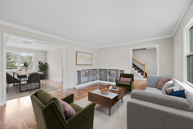 living room with crown molding, stairway, light wood-style flooring, and baseboards