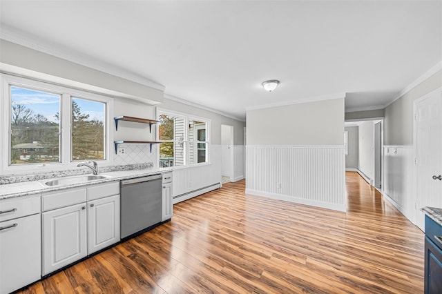 kitchen with a wainscoted wall, a sink, light wood-style floors, stainless steel dishwasher, and baseboard heating