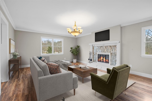 living room with baseboards, ornamental molding, wood finished floors, a notable chandelier, and a glass covered fireplace