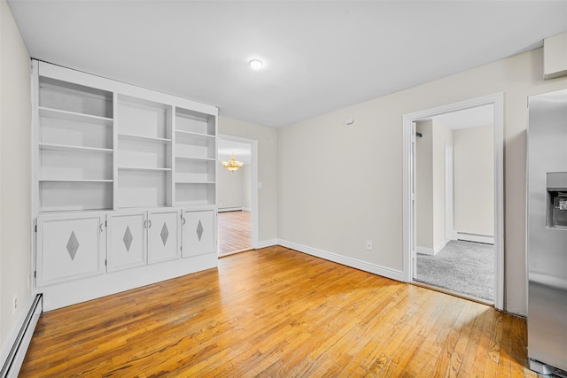 interior space featuring a baseboard heating unit, a notable chandelier, baseboards, and light wood finished floors