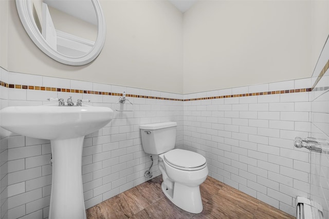 bathroom with a baseboard heating unit, tile walls, toilet, and wainscoting