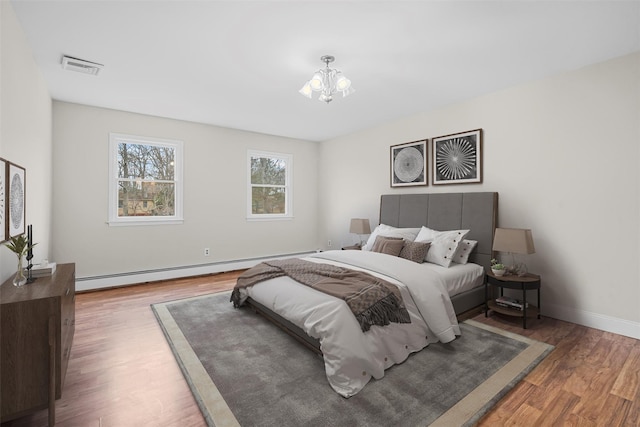 bedroom featuring visible vents, baseboards, a chandelier, baseboard heating, and wood finished floors