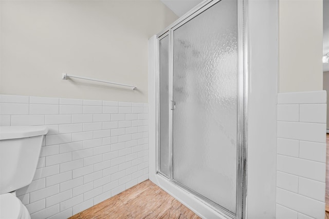 full bathroom featuring tile walls, toilet, a wainscoted wall, and a stall shower