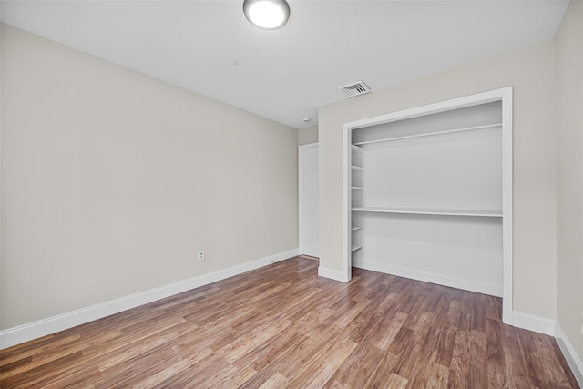 unfurnished bedroom with a closet, visible vents, baseboards, and wood finished floors