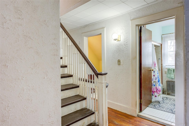 staircase with baseboards, wood finished floors, radiator heating unit, and a textured wall