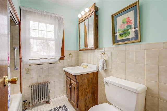 bathroom featuring radiator, toilet, vanity, wainscoting, and tile walls