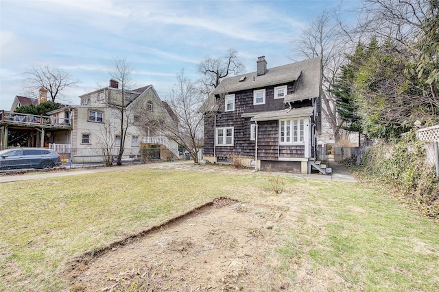 back of house with a shingled roof, a yard, fence, and a chimney