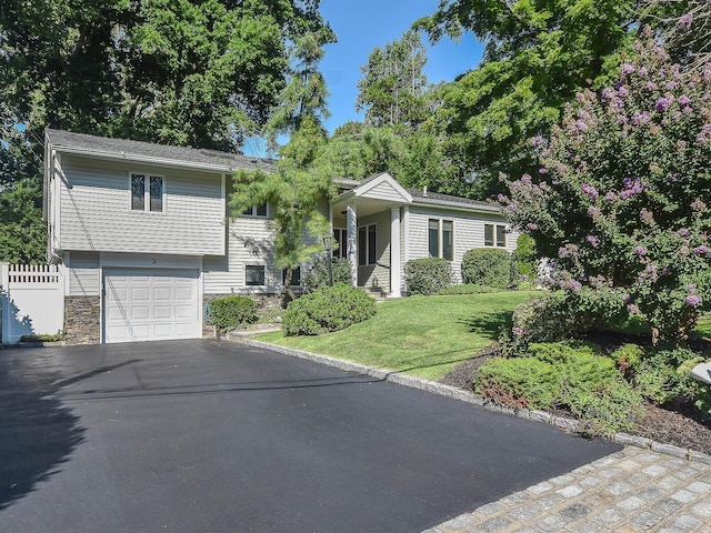 view of front facade featuring aphalt driveway, a front yard, fence, a garage, and stone siding