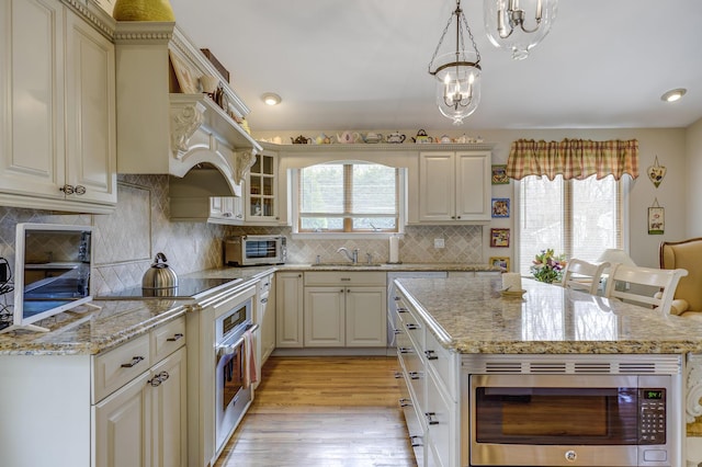 kitchen with stainless steel microwave, a sink, light stone countertops, light wood-type flooring, and black electric cooktop