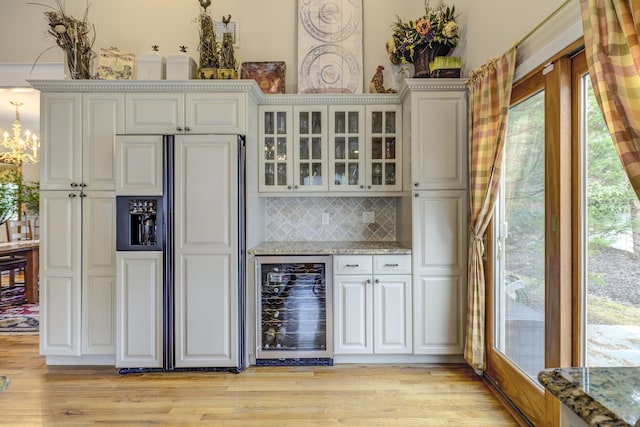 bar with light wood-type flooring, wine cooler, paneled fridge, and backsplash