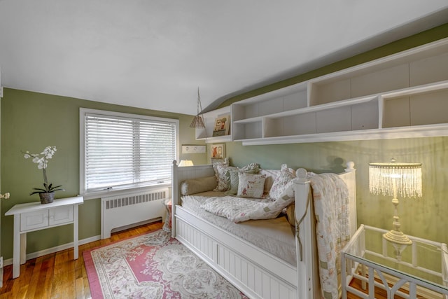 bedroom featuring lofted ceiling, baseboards, wood finished floors, and radiator