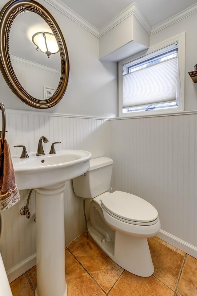 half bathroom with toilet, tile patterned floors, crown molding, and wainscoting