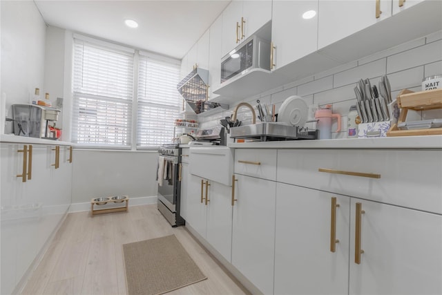 kitchen featuring light wood finished floors, tasteful backsplash, baseboards, white cabinets, and appliances with stainless steel finishes