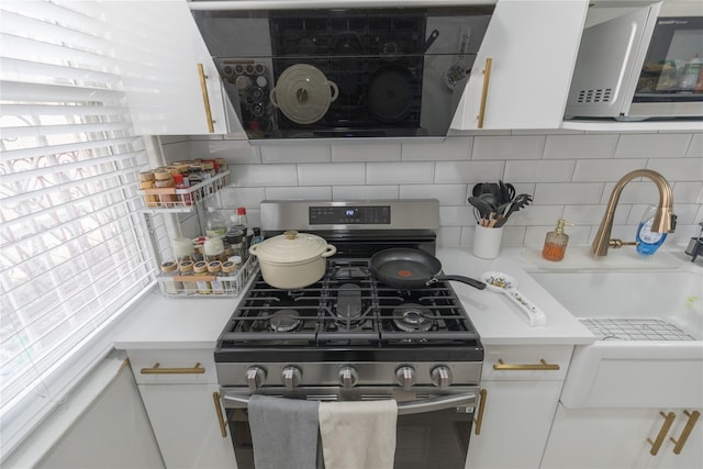 kitchen with stainless steel appliances, a sink, white cabinets, light countertops, and decorative backsplash