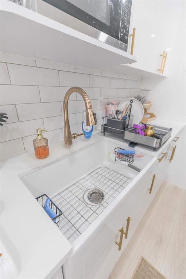 interior details featuring light countertops, white cabinetry, a sink, and backsplash