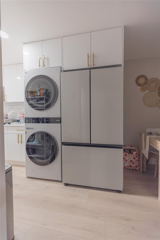 laundry area with stacked washer and dryer, cabinet space, and light wood-style flooring