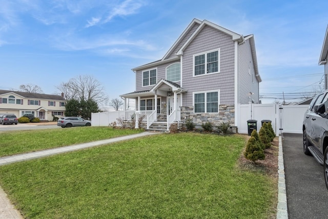 view of front of home with stone siding, a front yard, fence, and a gate