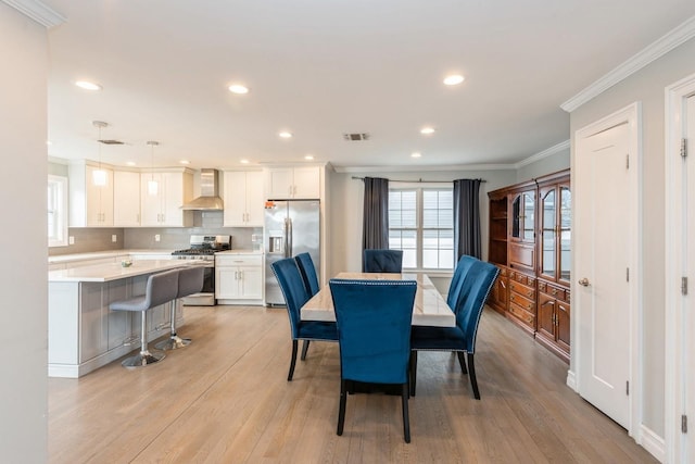 dining space with light wood-style floors, plenty of natural light, visible vents, and crown molding