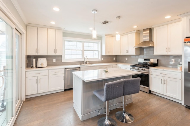 kitchen with a kitchen island, a sink, visible vents, appliances with stainless steel finishes, and wall chimney exhaust hood