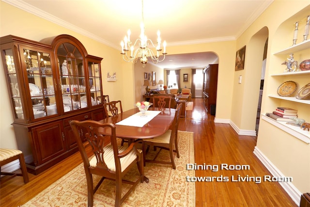 dining room with arched walkways, a notable chandelier, wood finished floors, baseboards, and crown molding