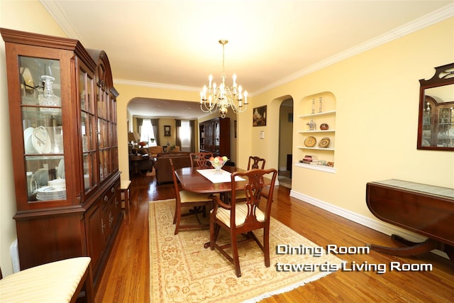 dining space with built in shelves, arched walkways, a notable chandelier, crown molding, and wood finished floors