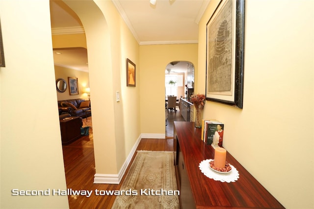 corridor featuring baseboards, crown molding, arched walkways, and wood finished floors