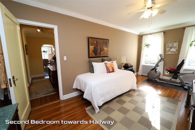 bedroom featuring baseboards, arched walkways, wood finished floors, and ornamental molding