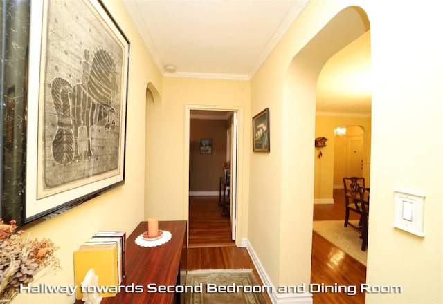 hallway with arched walkways, baseboards, wood finished floors, and crown molding